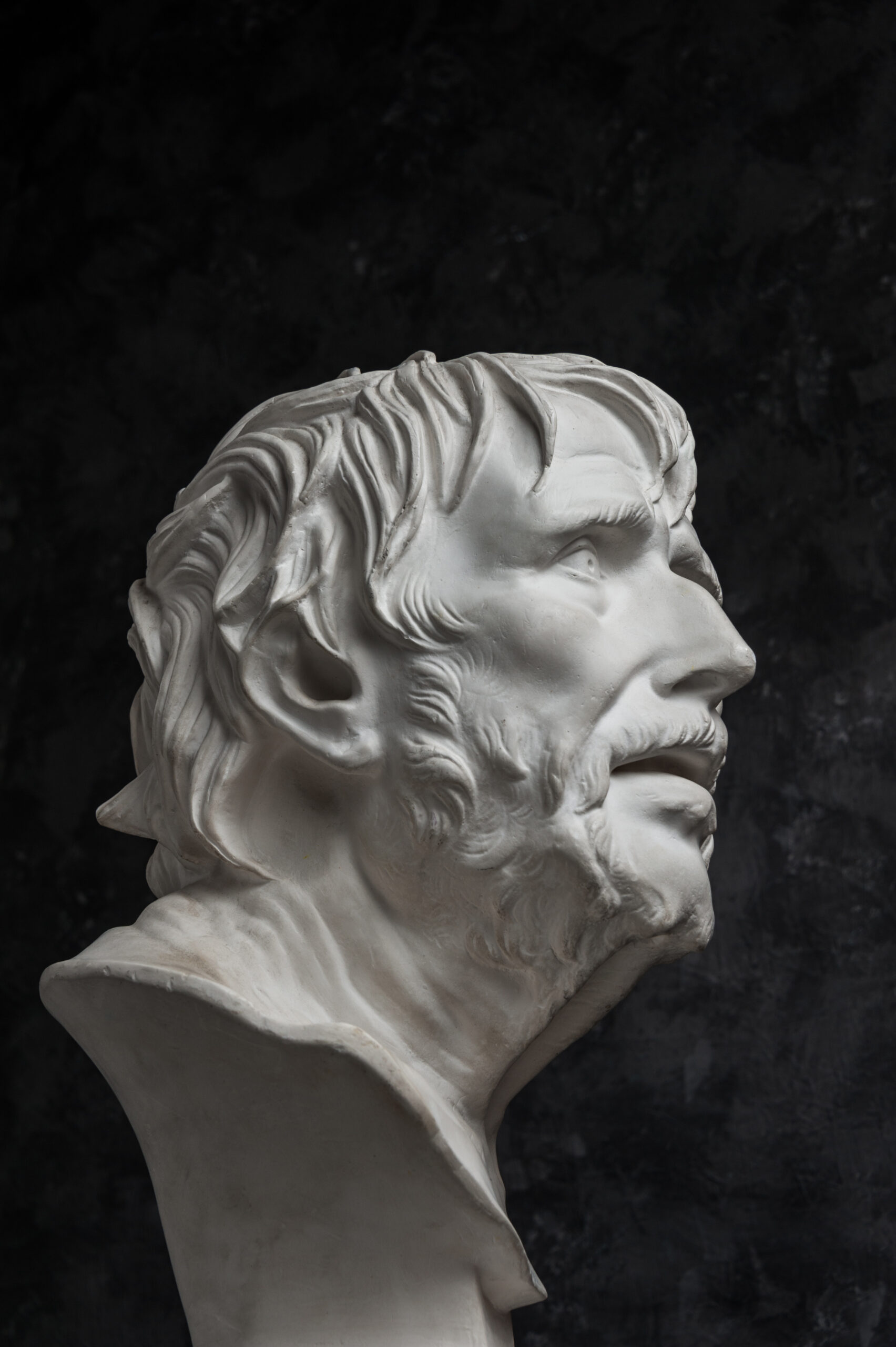 Gypsum copy of ancient statue Seneca head on dark textured background. Plaster sculpture man face.